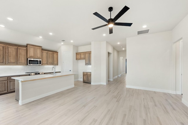 kitchen with ceiling fan, sink, stainless steel appliances, light hardwood / wood-style floors, and a kitchen island with sink