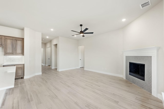 unfurnished living room with light hardwood / wood-style floors, ceiling fan, and a tiled fireplace