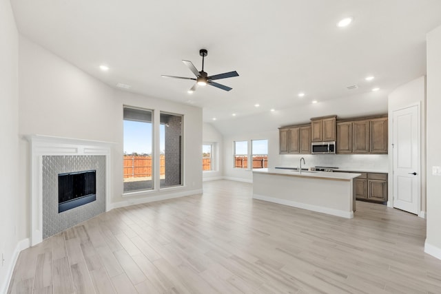 kitchen with a kitchen island with sink, sink, ceiling fan, light wood-type flooring, and a tiled fireplace