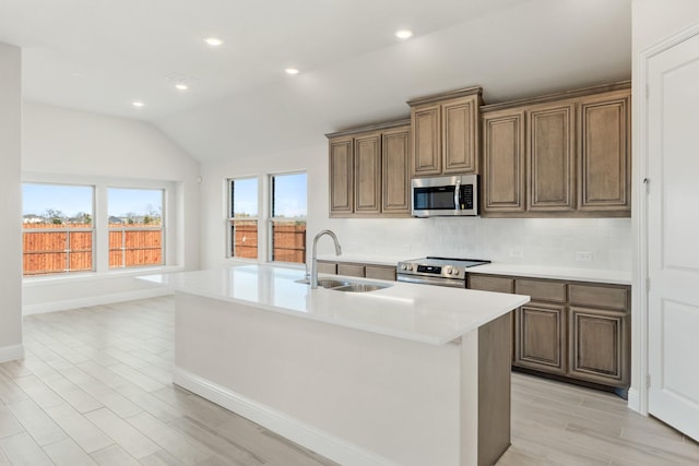 kitchen featuring sink, stainless steel appliances, an island with sink, lofted ceiling, and light wood-type flooring