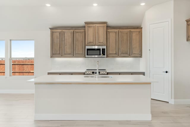 kitchen featuring sink, backsplash, an island with sink, light hardwood / wood-style floors, and vaulted ceiling