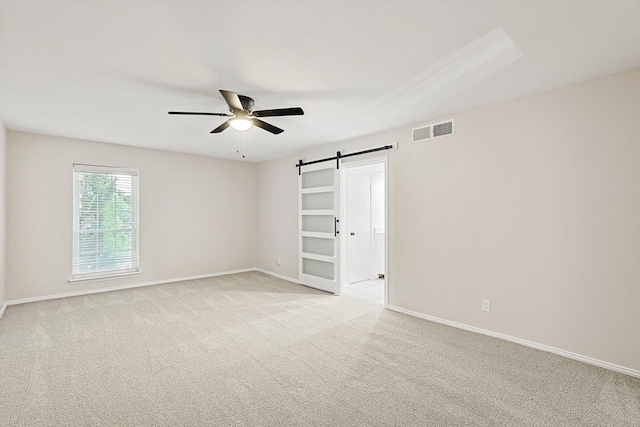 empty room featuring ceiling fan, a barn door, and light carpet