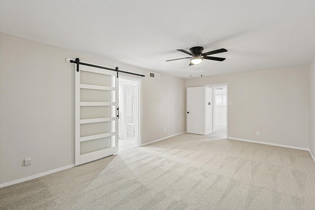 carpeted empty room featuring ceiling fan and a barn door