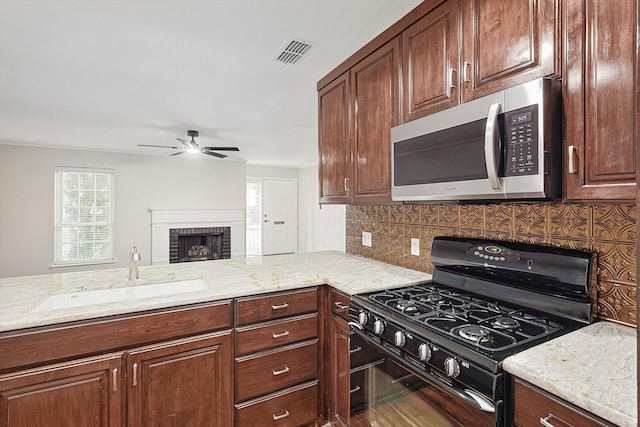 kitchen with sink, decorative backsplash, light stone countertops, a fireplace, and black gas range oven