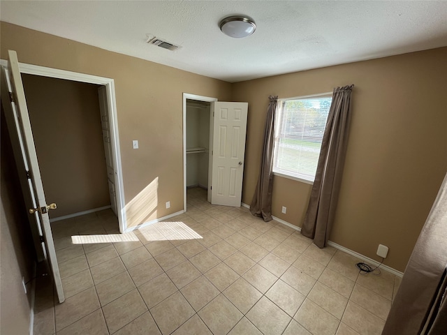 unfurnished bedroom with a textured ceiling, a spacious closet, a closet, and light tile patterned flooring