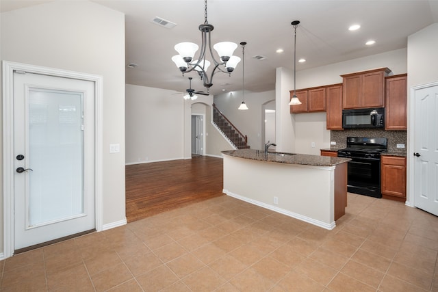 kitchen with pendant lighting, light hardwood / wood-style floors, a kitchen island with sink, black appliances, and ceiling fan with notable chandelier