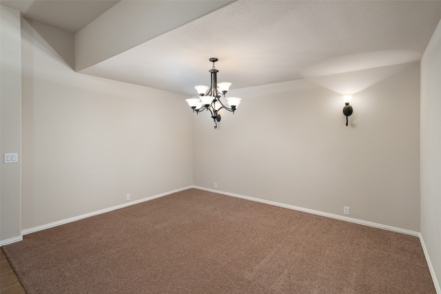 spare room featuring dark colored carpet and a notable chandelier