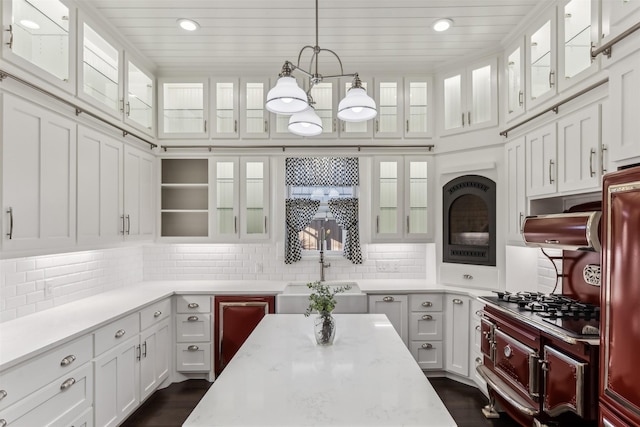 kitchen featuring decorative light fixtures, white cabinetry, sink, backsplash, and light stone countertops