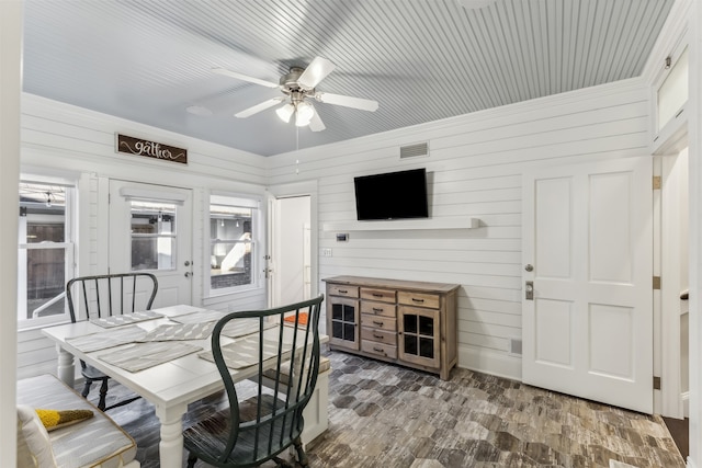 dining area featuring ceiling fan, wood walls, and wood-type flooring