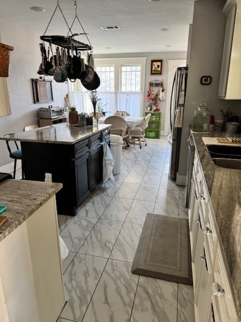 kitchen featuring a kitchen island, stone countertops, a breakfast bar, sink, and stainless steel fridge