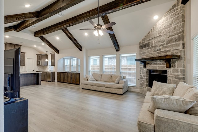 living room featuring a fireplace, lofted ceiling with beams, ceiling fan, and light wood-type flooring