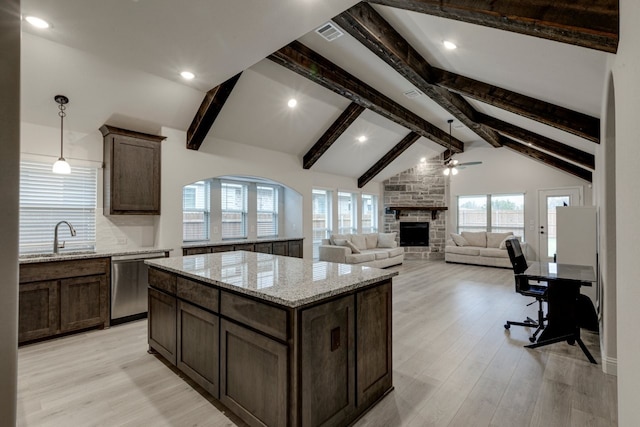 kitchen with sink, dishwasher, a kitchen island, a fireplace, and light stone countertops