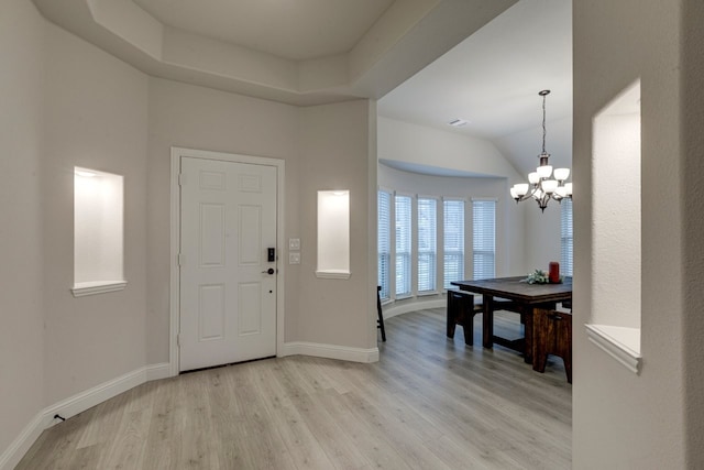 foyer entrance with light wood-type flooring, an inviting chandelier, and a tray ceiling