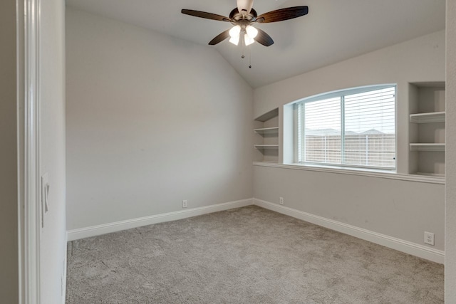 spare room featuring built in shelves, light colored carpet, ceiling fan, and vaulted ceiling