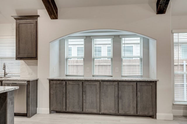 interior space with beamed ceiling, stainless steel dishwasher, dark brown cabinetry, and light stone countertops