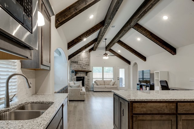 kitchen featuring a stone fireplace, sink, light stone countertops, beam ceiling, and light hardwood / wood-style flooring