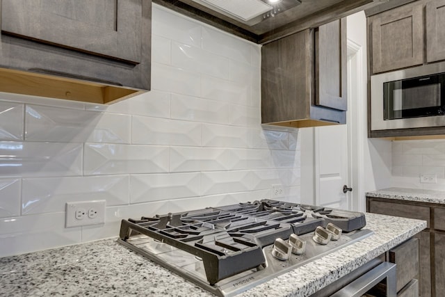 kitchen with tasteful backsplash, light stone counters, black microwave, and stainless steel gas stovetop