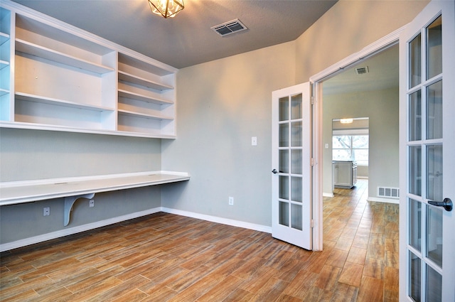 unfurnished office with hardwood / wood-style flooring, built in desk, and french doors