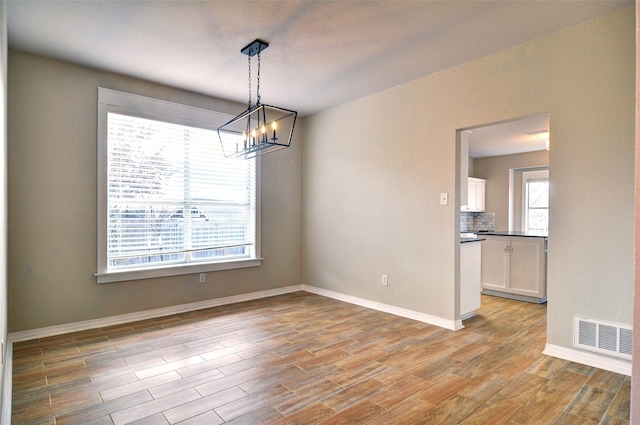 unfurnished dining area featuring a notable chandelier and light wood-type flooring