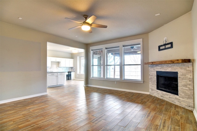 unfurnished living room featuring a fireplace, a textured ceiling, light wood-type flooring, and ceiling fan