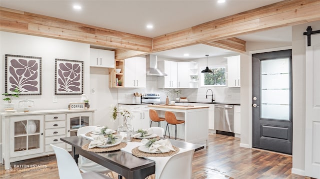 kitchen featuring wall chimney exhaust hood, stainless steel appliances, pendant lighting, a barn door, and white cabinetry