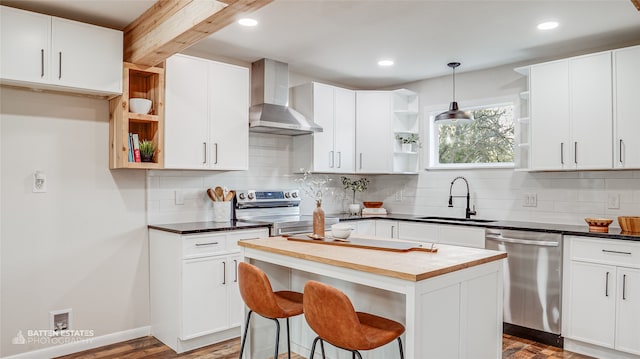 kitchen with white cabinets, sink, wall chimney exhaust hood, appliances with stainless steel finishes, and a kitchen island