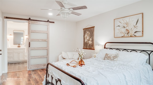 bedroom featuring light wood-type flooring, ensuite bath, ceiling fan, and a barn door