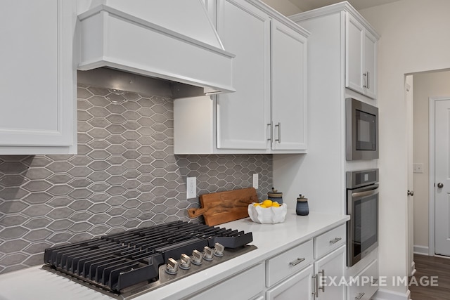 kitchen featuring tasteful backsplash, white cabinetry, stainless steel appliances, and custom range hood