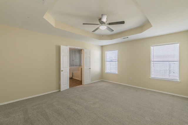 unfurnished bedroom featuring a raised ceiling, ensuite bathroom, carpet, and ceiling fan