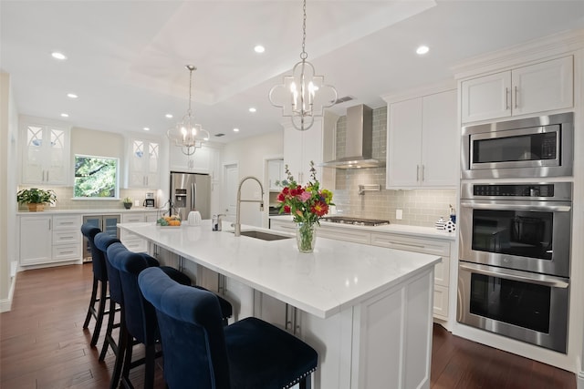 kitchen featuring a sink, wall chimney range hood, white cabinets, and stainless steel appliances