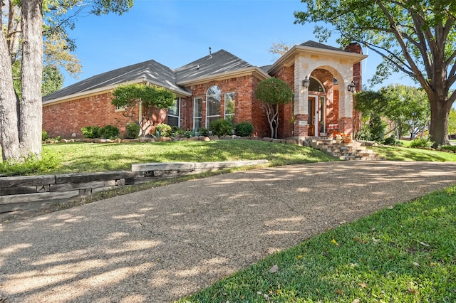 view of front of property featuring brick siding, a chimney, and a front yard