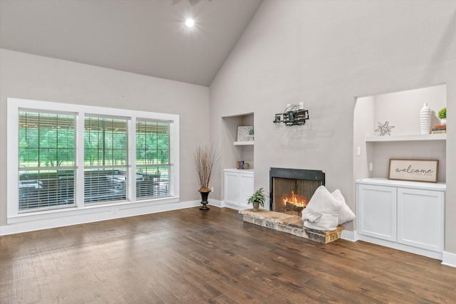 living room with built in shelves, a fireplace, high vaulted ceiling, and dark wood-type flooring