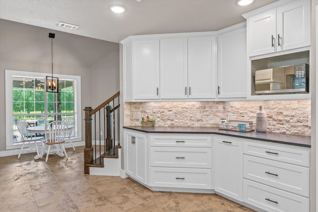 kitchen featuring white cabinetry, tasteful backsplash, a notable chandelier, pendant lighting, and lofted ceiling