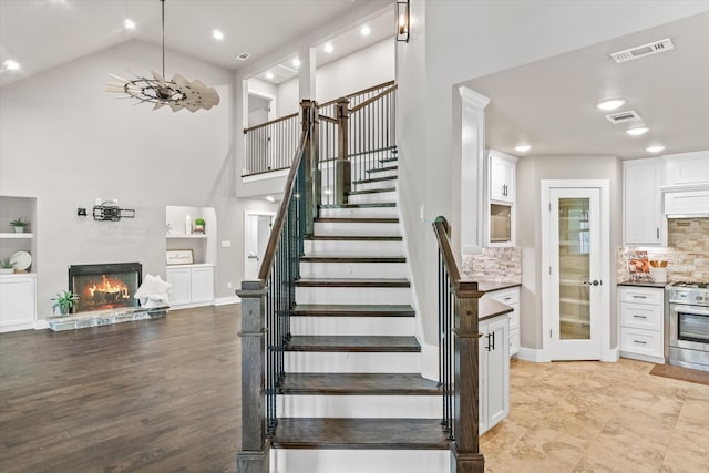 staircase with a stone fireplace, high vaulted ceiling, and wood-type flooring