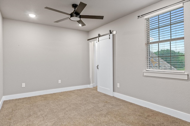 unfurnished bedroom with carpet flooring, a barn door, and ceiling fan