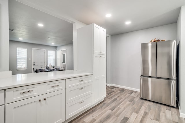 kitchen featuring light wood-type flooring, white cabinetry, kitchen peninsula, and stainless steel refrigerator