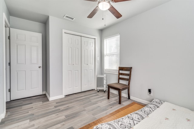 bedroom featuring ceiling fan, light hardwood / wood-style floors, radiator, and a closet