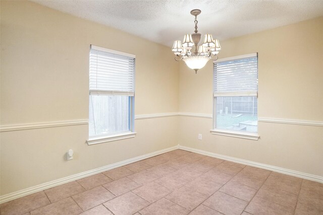 empty room with a wealth of natural light, light tile patterned flooring, a textured ceiling, and a notable chandelier