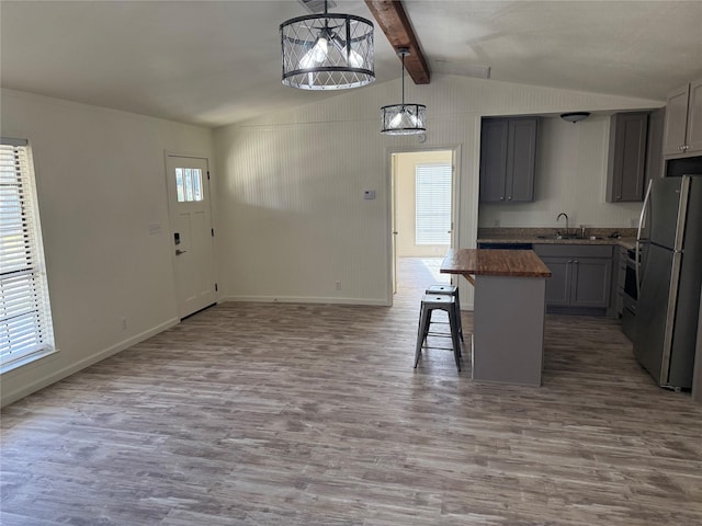 kitchen with butcher block counters, decorative light fixtures, stainless steel refrigerator, gray cabinets, and a kitchen island