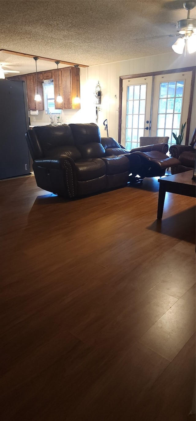 living room featuring ceiling fan, dark wood-type flooring, french doors, and a textured ceiling