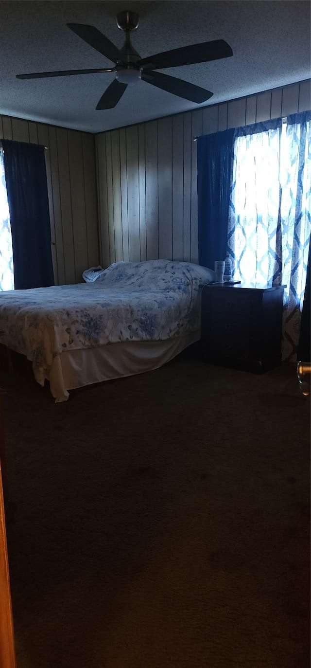 unfurnished bedroom with a textured ceiling, ceiling fan, carpet floors, and wood walls