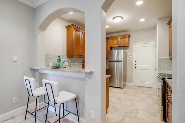 kitchen featuring a breakfast bar, tasteful backsplash, sink, light stone counters, and stainless steel appliances