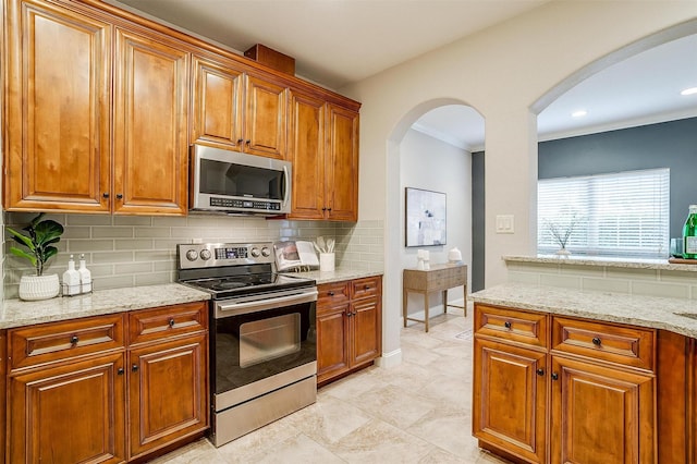 kitchen featuring light stone counters, decorative backsplash, stainless steel appliances, and crown molding