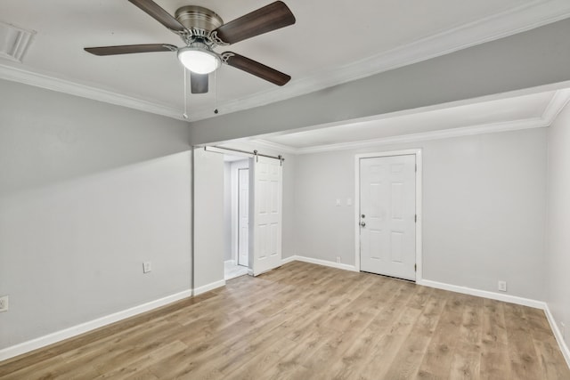 empty room featuring ceiling fan, a barn door, light wood-type flooring, and crown molding