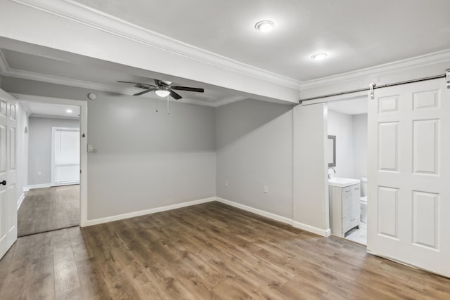 interior space featuring ceiling fan, a barn door, wood-type flooring, and ornamental molding