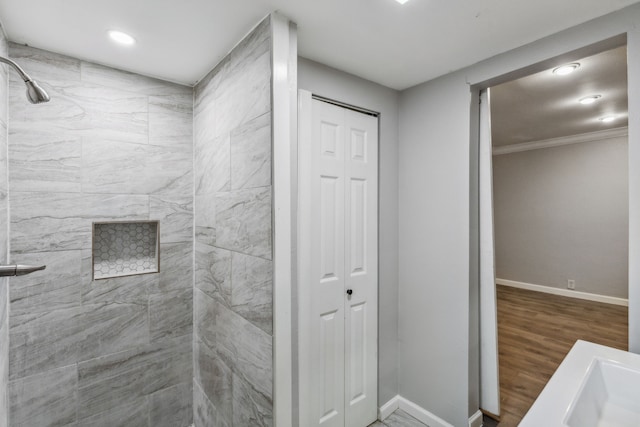 bathroom featuring a tile shower, hardwood / wood-style flooring, ornamental molding, and sink