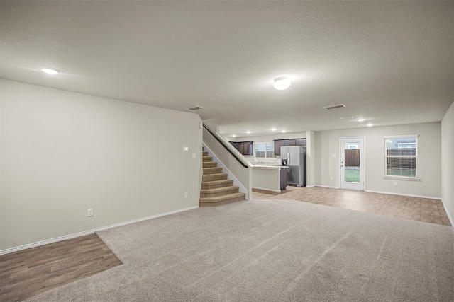 basement with a textured ceiling, light hardwood / wood-style flooring, and stainless steel refrigerator with ice dispenser