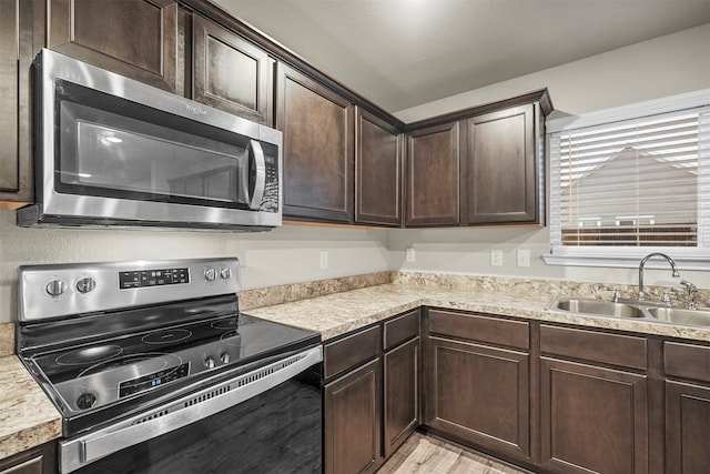 kitchen with sink, light wood-type flooring, dark brown cabinets, and appliances with stainless steel finishes