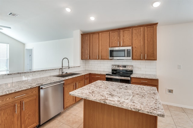 kitchen with lofted ceiling, sink, light stone countertops, appliances with stainless steel finishes, and a kitchen island