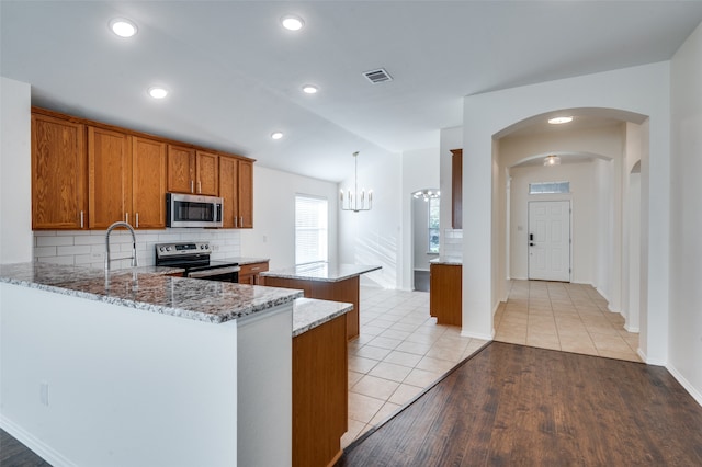 kitchen with light stone countertops, appliances with stainless steel finishes, kitchen peninsula, decorative backsplash, and light hardwood / wood-style floors